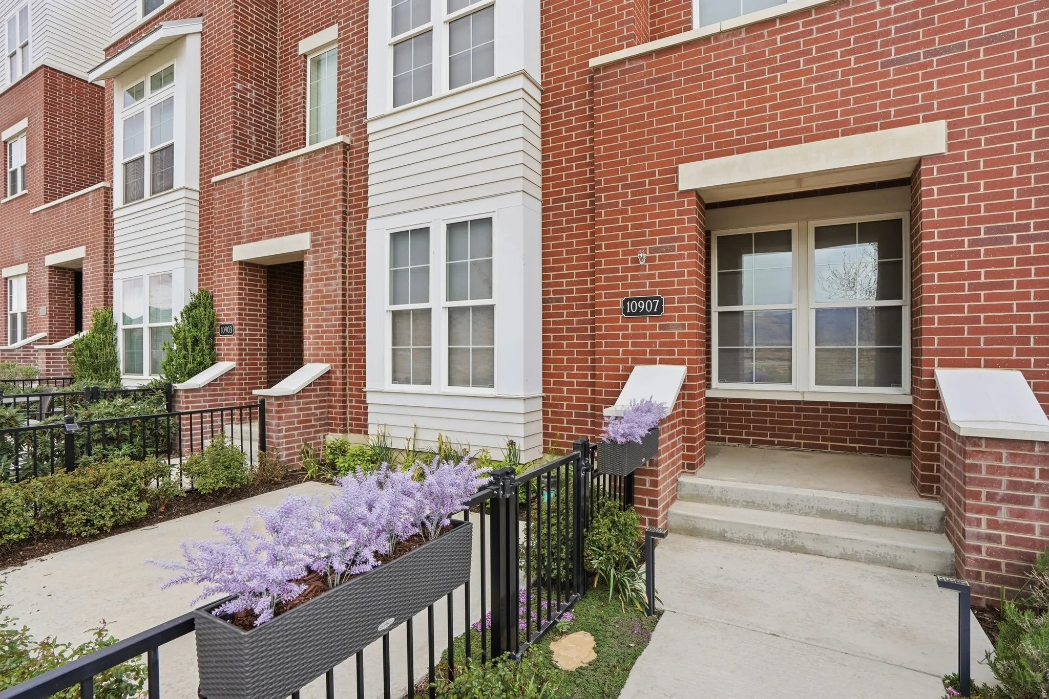 Red brick townhome facade featuring a prominent address plaque, white-trimmed windows, a covered entry, and a concrete walkway