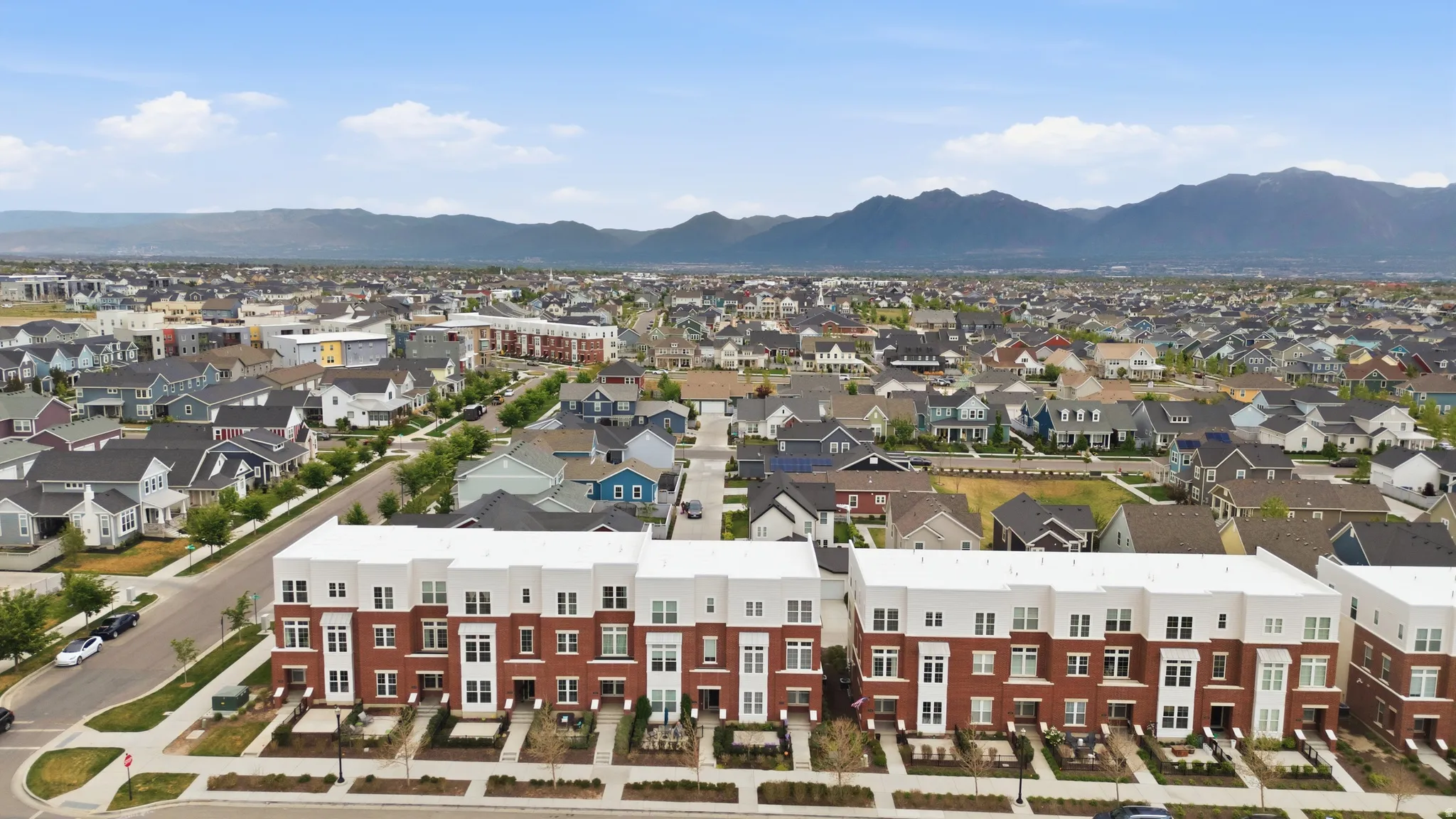 Modern townhome community featuring brick and white facade, integrated landscaping, and mountain backdrop
