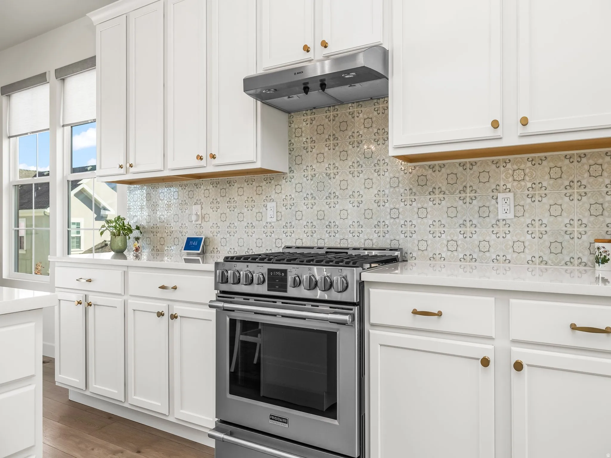 Kitchen with decorative backsplash, stainless steel gas stove, white cabinetry, under cabinet range hood, and light stone counters