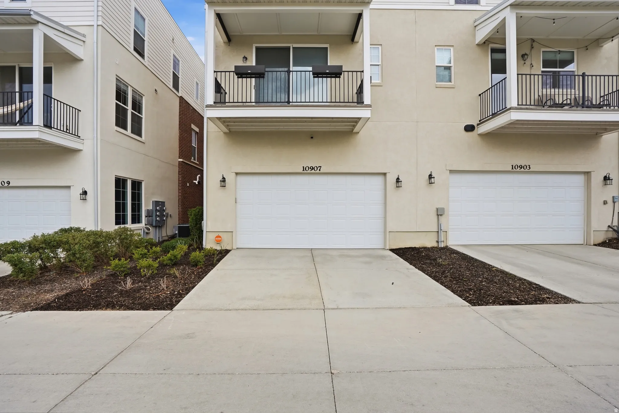 Exterior featuring two-car garage with concrete driveway, balconies with black iron railings, and sconce lighting