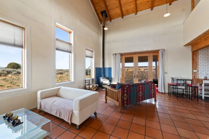 Tiled living area featuring a wood stove, high vaulted ceiling, and a wood ceiling with exposed beams