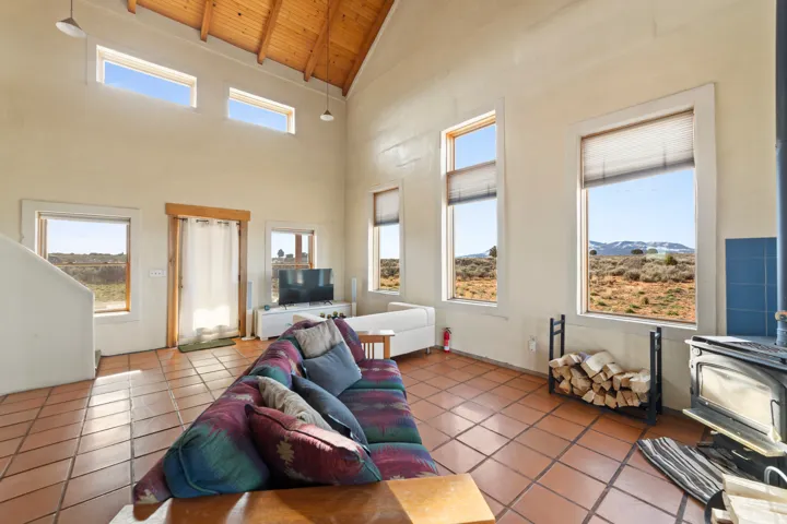 Living room with a wood stove, high vaulted ceiling, a wooden ceiling with exposed beams, and tile patterned floors