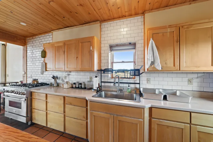 Kitchen with light countertops, stainless steel stove, backsplash, wood ceiling, and light brown cabinetry