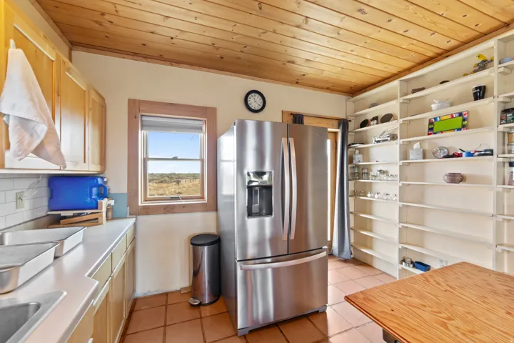 Kitchen with stainless steel fridge, wood ceiling, light tile patterned flooring, light countertops, and tasteful backsplash