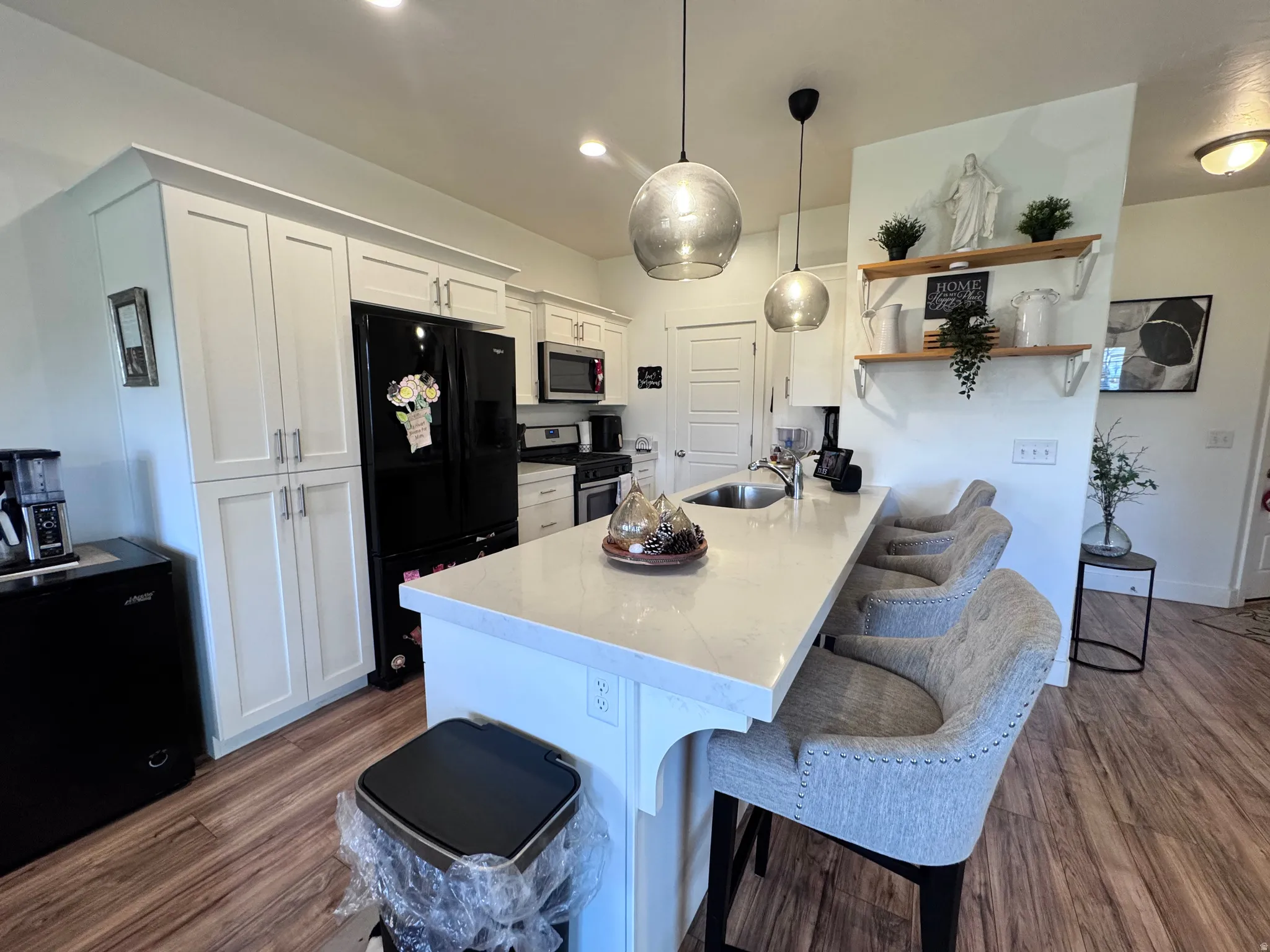 Kitchen featuring a kitchen breakfast bar, white cabinetry, dark wood-style flooring, stainless steel appliances, and hanging light fixtures