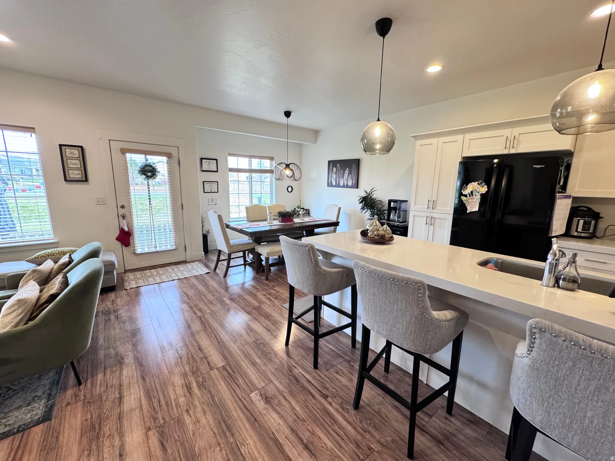 Kitchen with white cabinetry, a breakfast bar area, light stone counters, freestanding refrigerator, and dark wood-style flooring