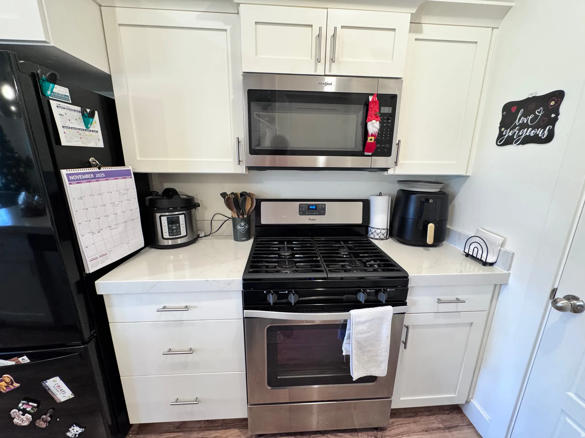 Kitchen with stainless steel appliances, white cabinets, light stone counters, and dark wood-style flooring