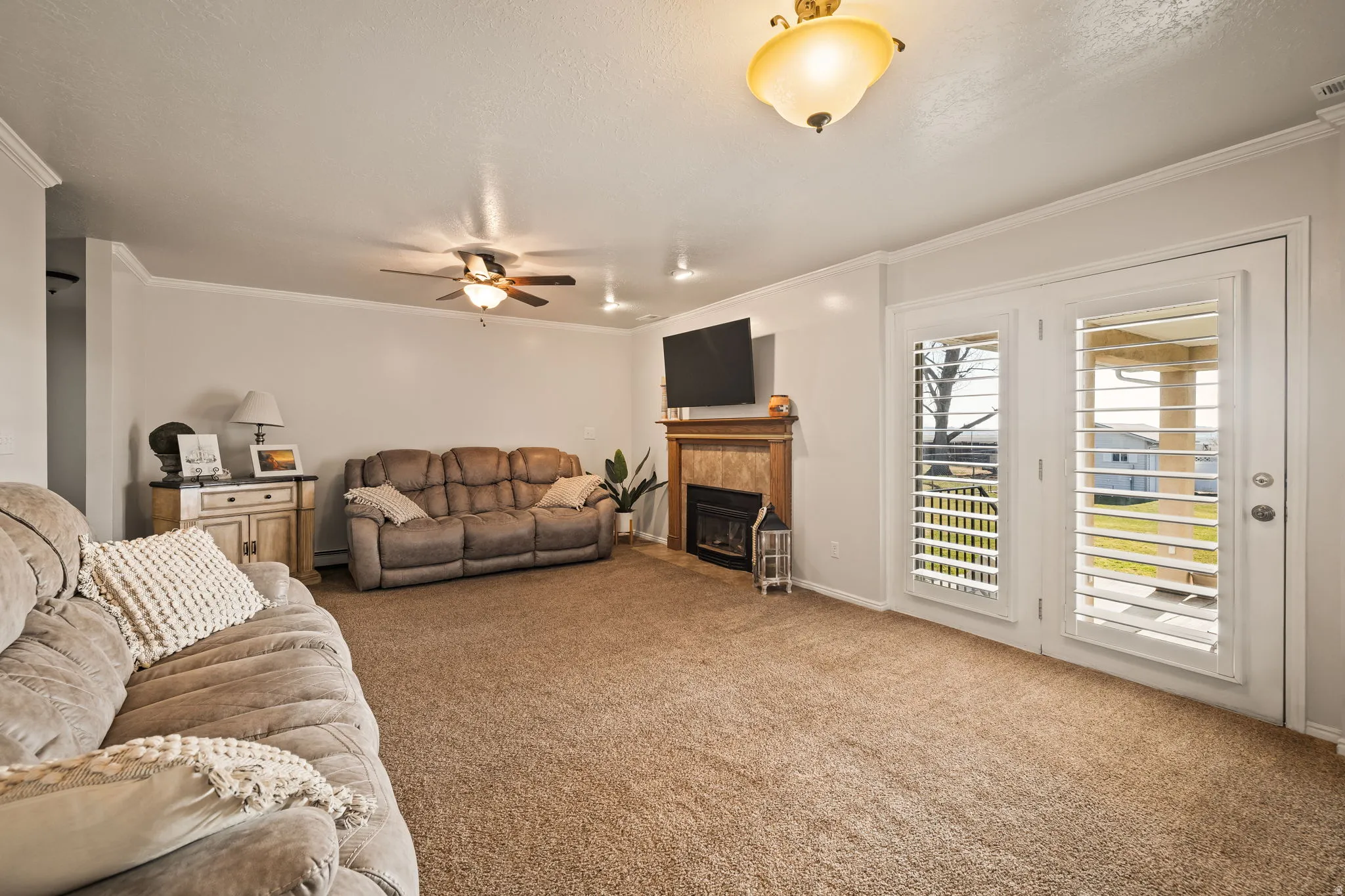 Living area featuring carpet floors, a fireplace, crown molding, a ceiling fan, and a baseboard radiator