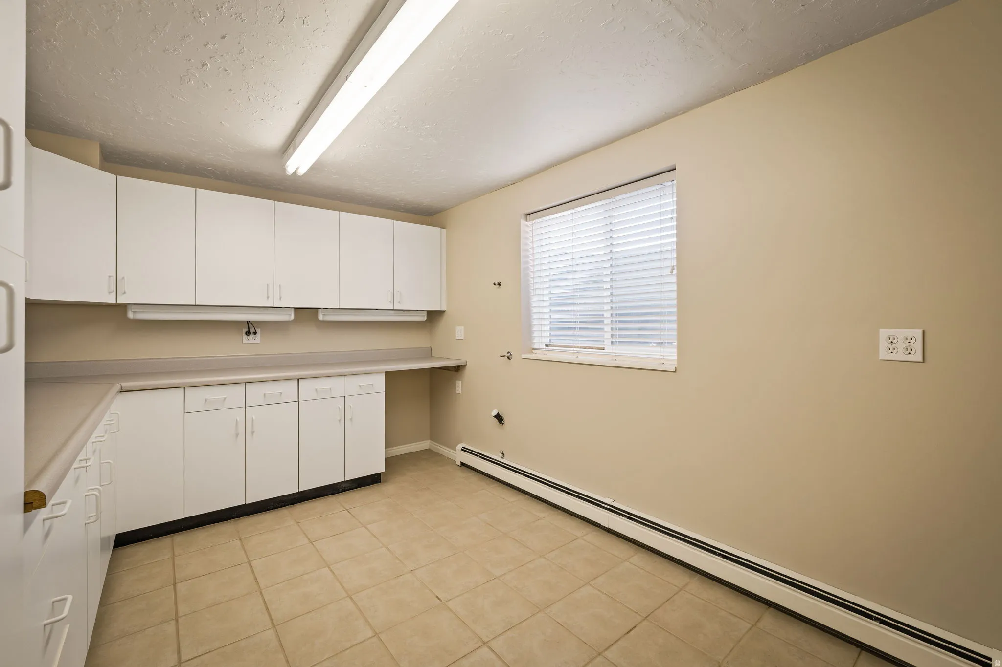 Kitchen featuring a baseboard radiator, light countertops, white cabinetry, a textured ceiling, and light tile patterned floors