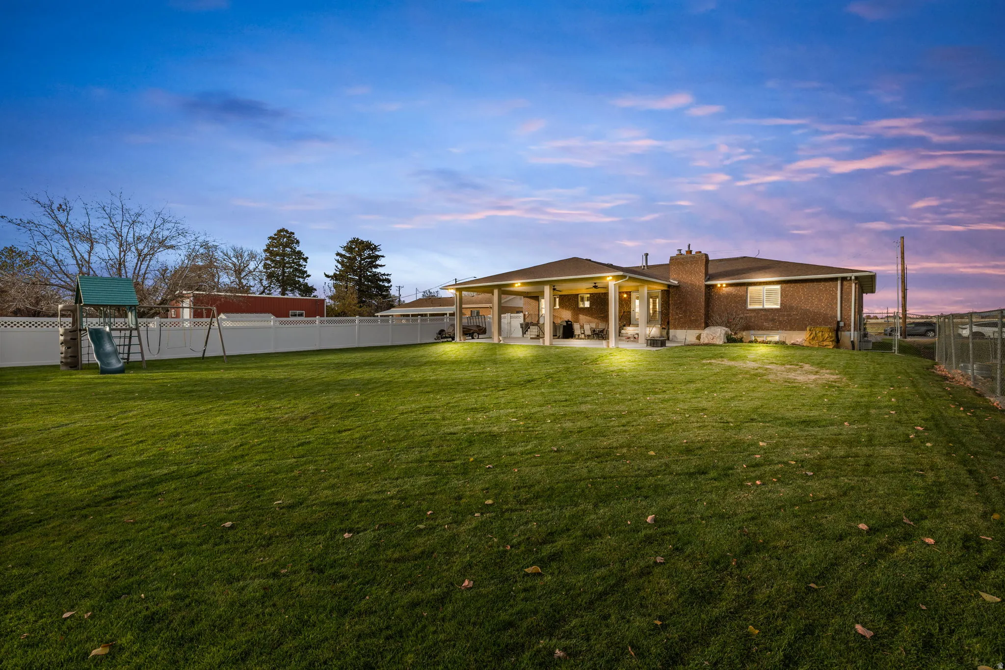 Back of property featuring a fenced backyard, a patio area, a chimney, a playground, and brick siding