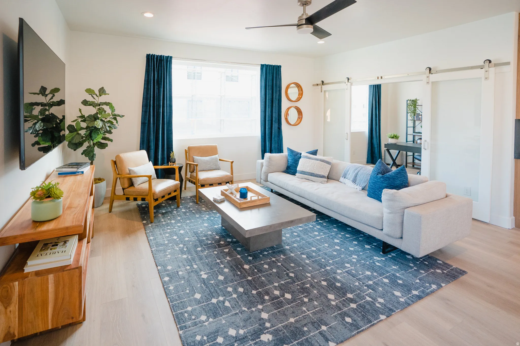 Living room with a barn door, light wood finished floors, ceiling fan, and recessed lighting