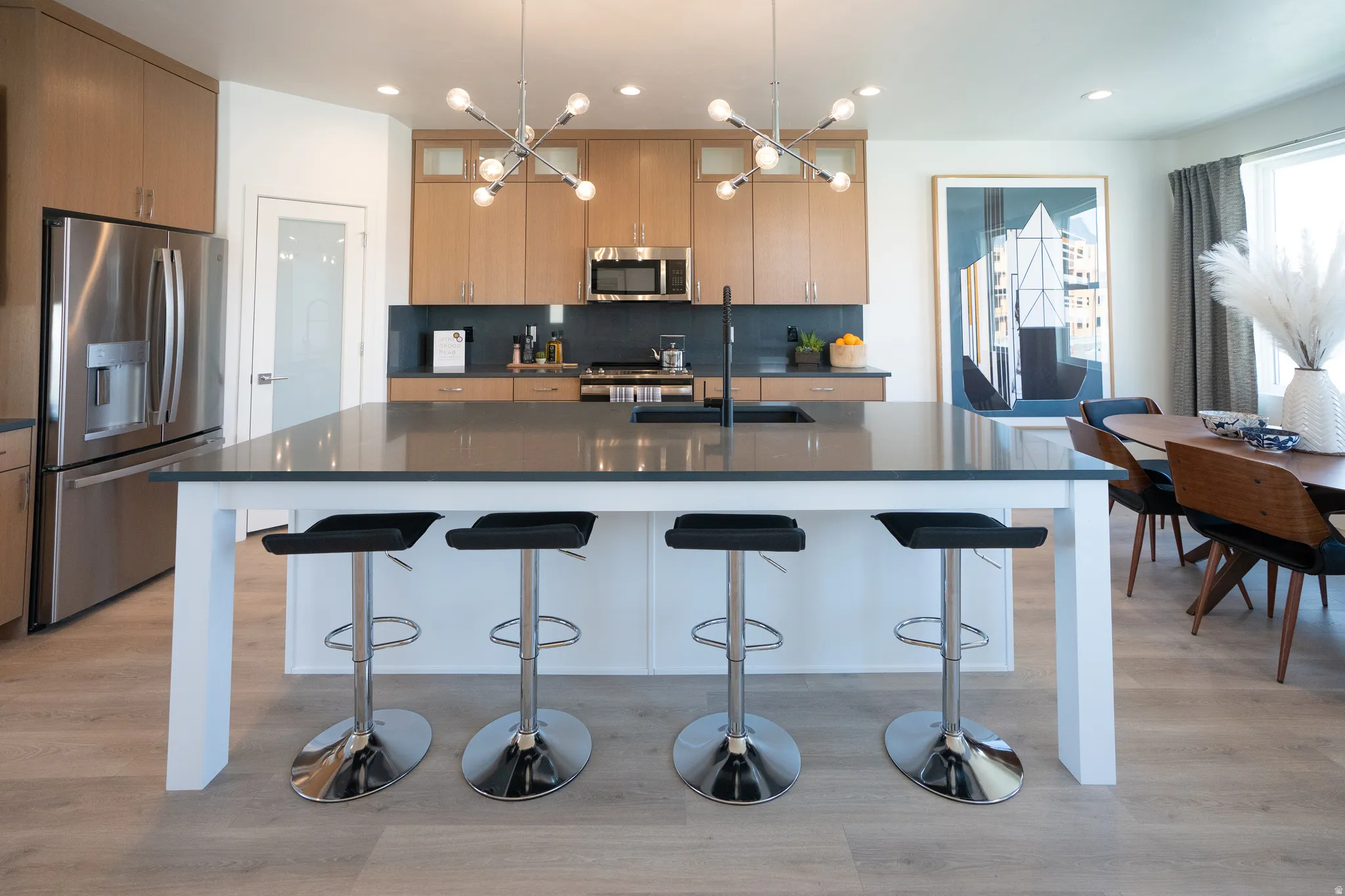 Kitchen with stainless steel appliances, an island with sink, light wood finished floors, decorative light fixtures, and recessed lighting