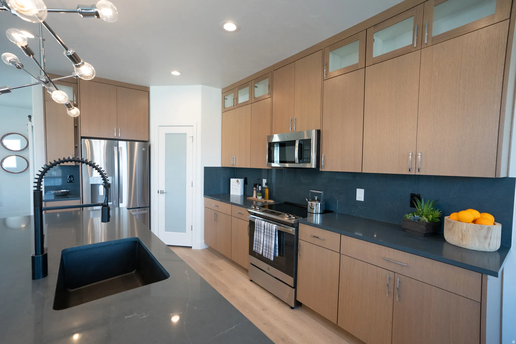 Kitchen featuring pendant lighting, stainless steel appliances, decorative backsplash, light wood finished floors, and glass insert cabinets
