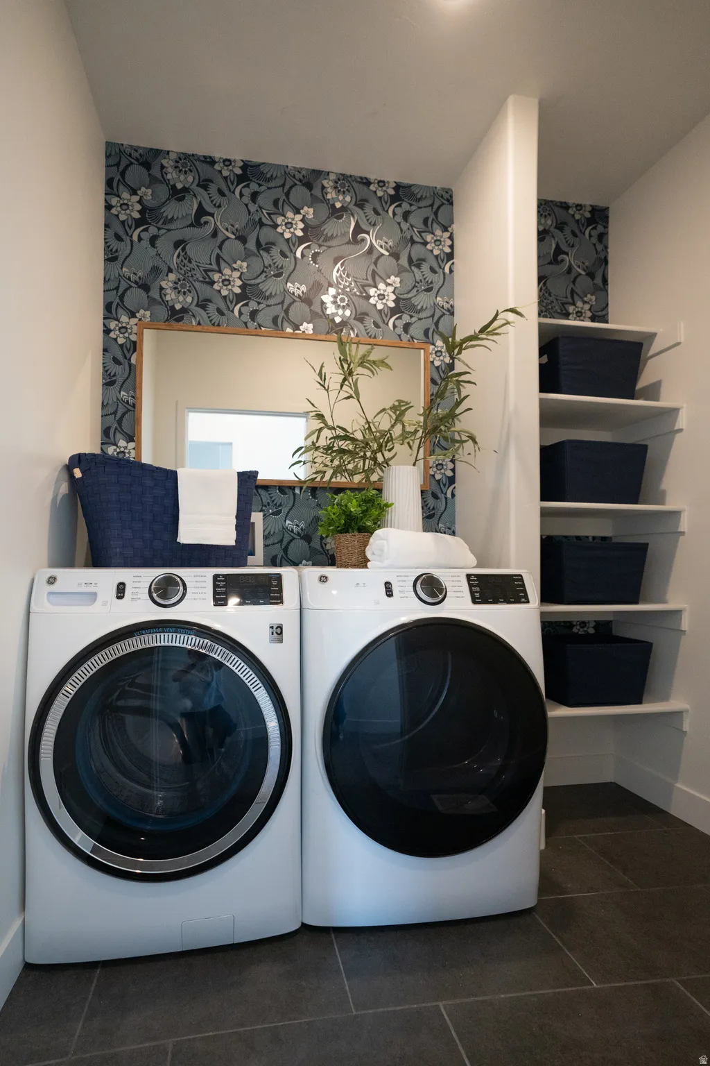 Laundry area with dark tile patterned floors, separate washer and dryer, and wallpapered walls