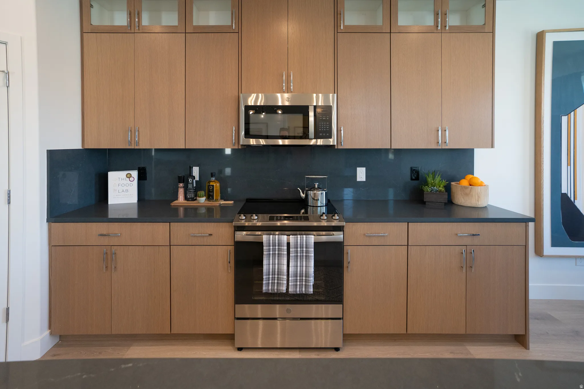 Kitchen featuring stainless steel appliances, glass insert cabinets, tasteful backsplash, and light wood-type flooring