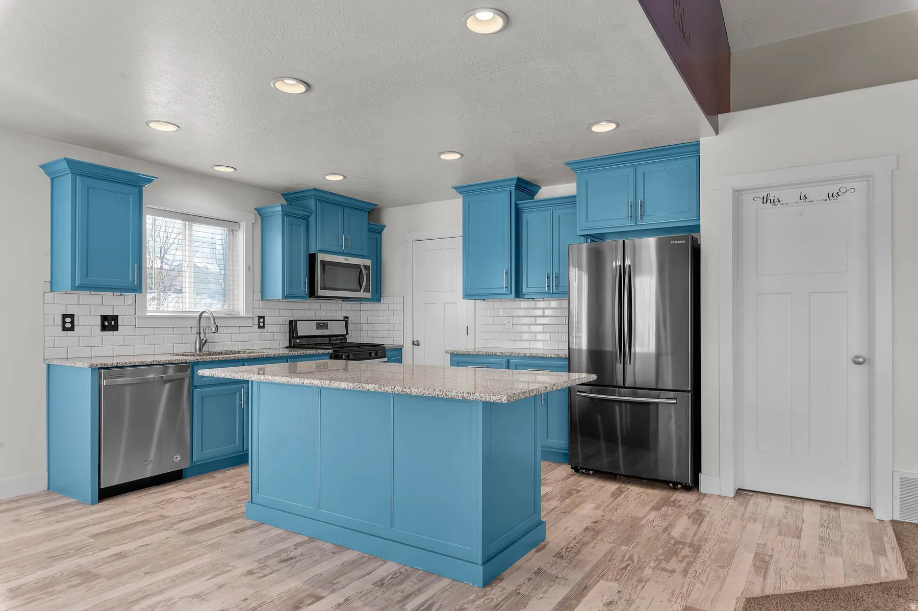 Kitchen with blue cabinetry, stainless steel appliances, light stone counters, recessed lighting, and a textured ceiling