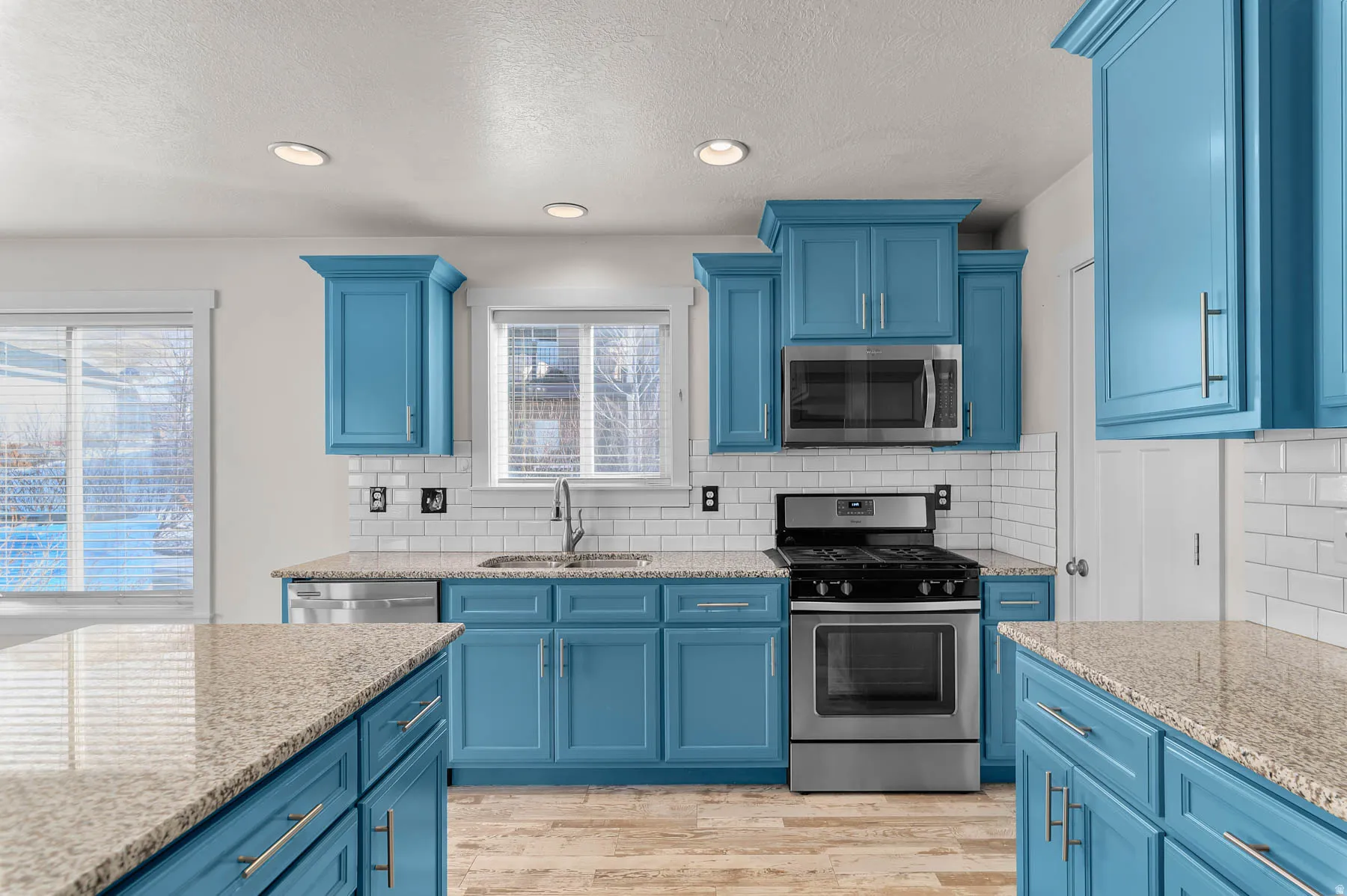 Kitchen with blue cabinetry, appliances with stainless steel finishes, light stone countertops, a textured ceiling, and recessed lighting