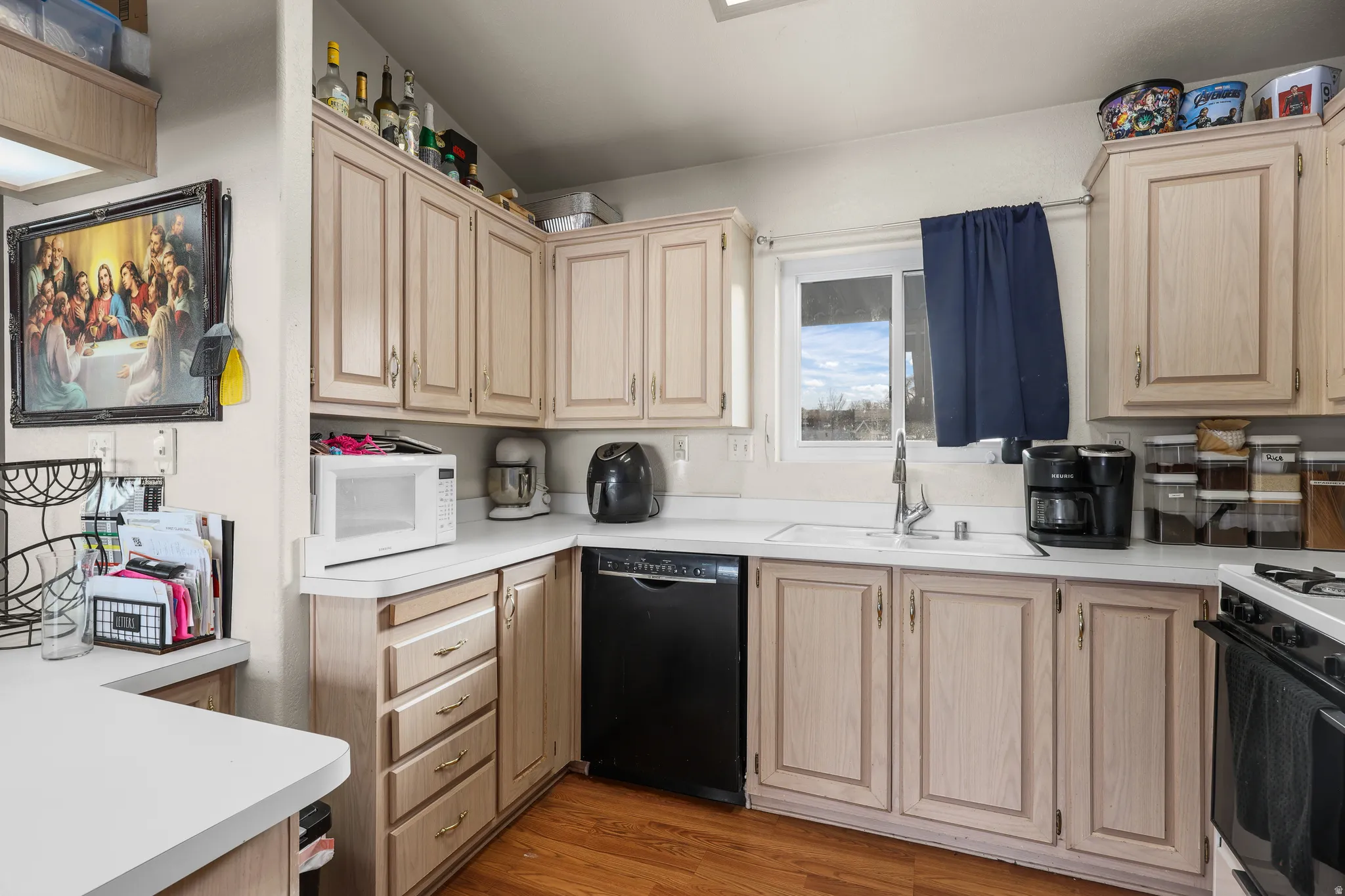 Kitchen with light brown cabinetry, light countertops, range with gas stovetop, and dishwasher