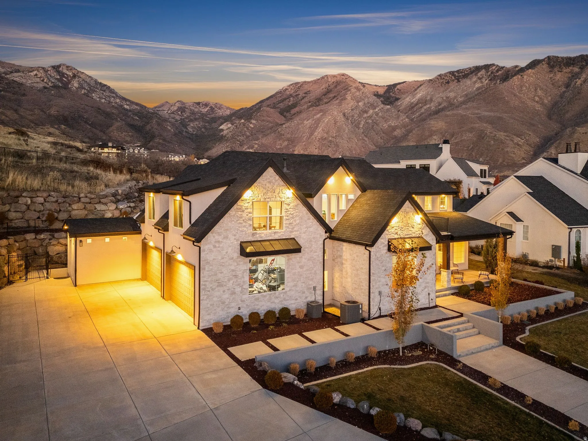 View of front of property featuring stone siding, a mountain view, concrete driveway, a garage, and a yard