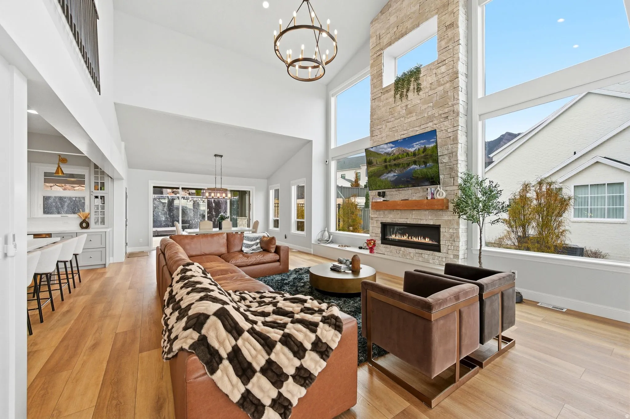 Living room with a chandelier, light wood-type flooring, a stone fireplace, and a towering ceiling