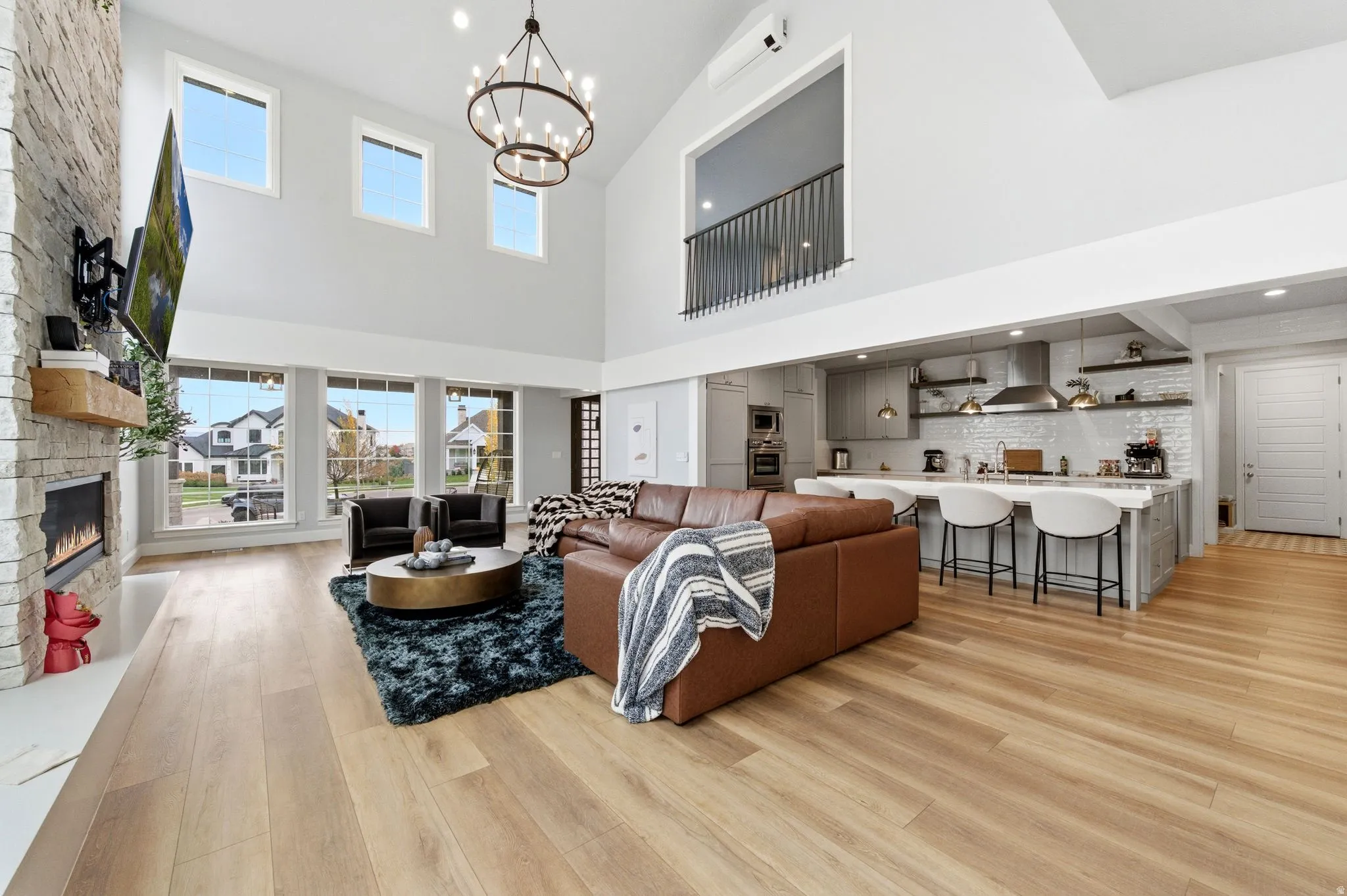 Living area featuring light wood-style flooring, a stone fireplace, a chandelier, recessed lighting, and a high ceiling