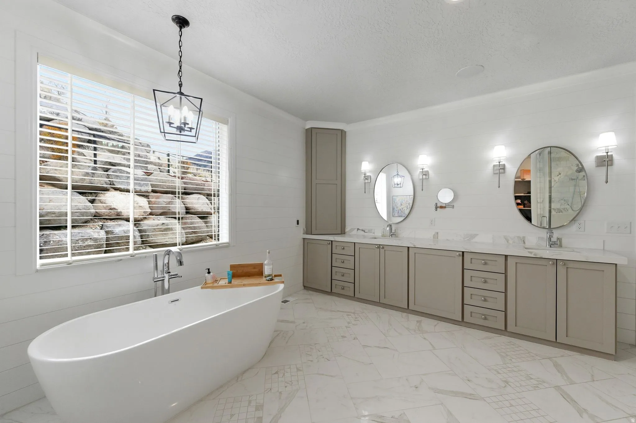Bathroom featuring double vanity, a soaking tub, light marble finish floors, a textured ceiling, and a chandelier