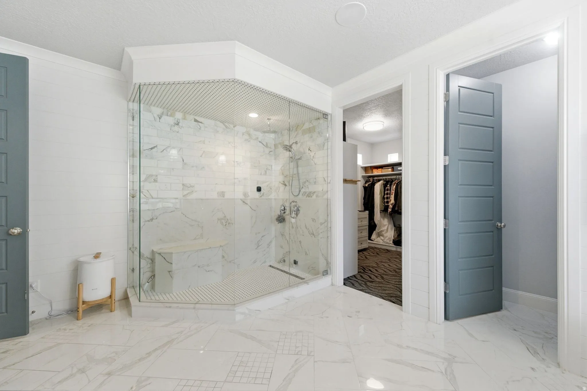 Bathroom featuring a spacious closet, a textured ceiling, a marble finish shower, and marble tiled flooring