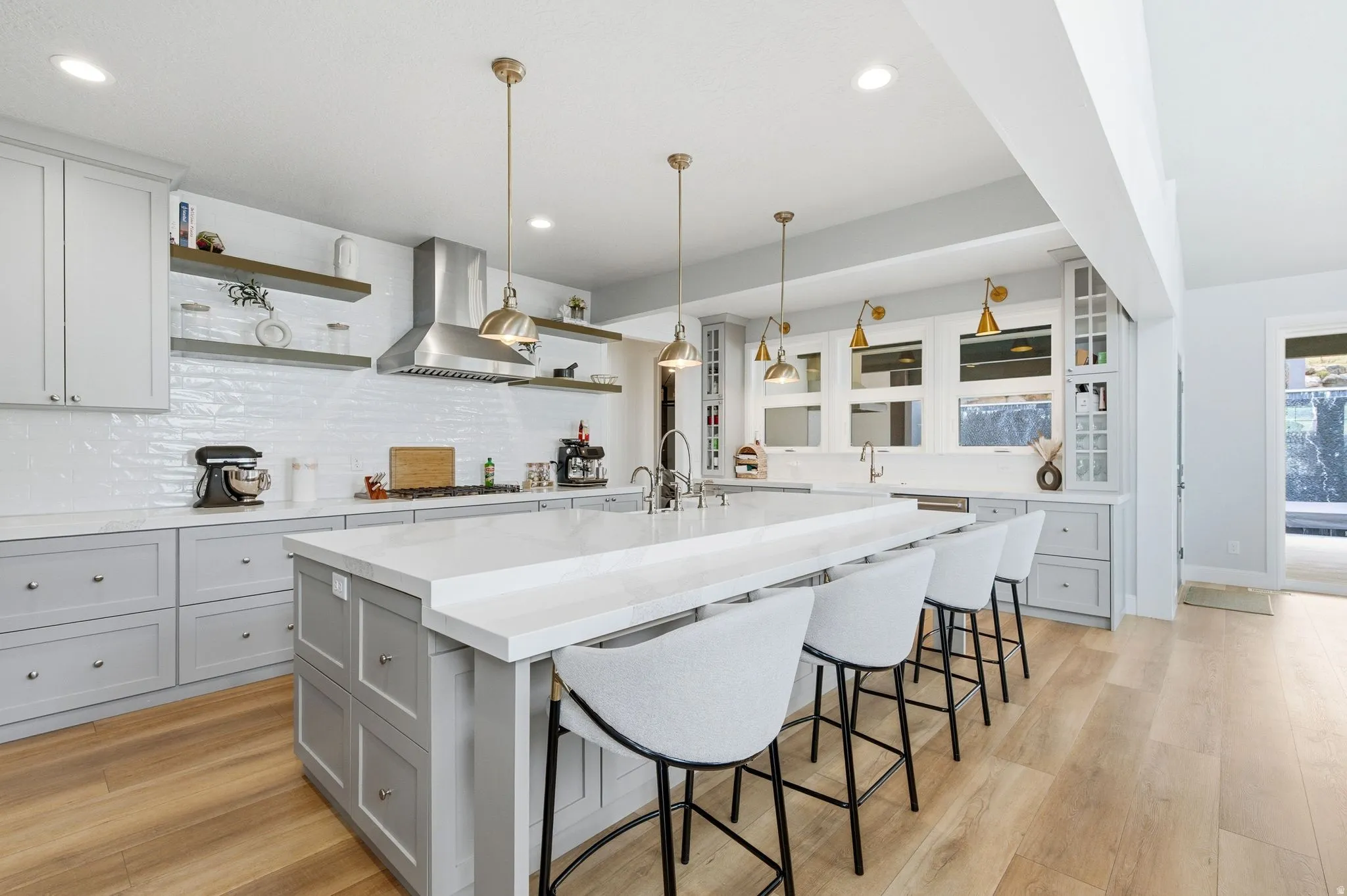 Kitchen featuring open shelves, a breakfast bar area, light stone counters, a large island with sink, and decorative light fixtures