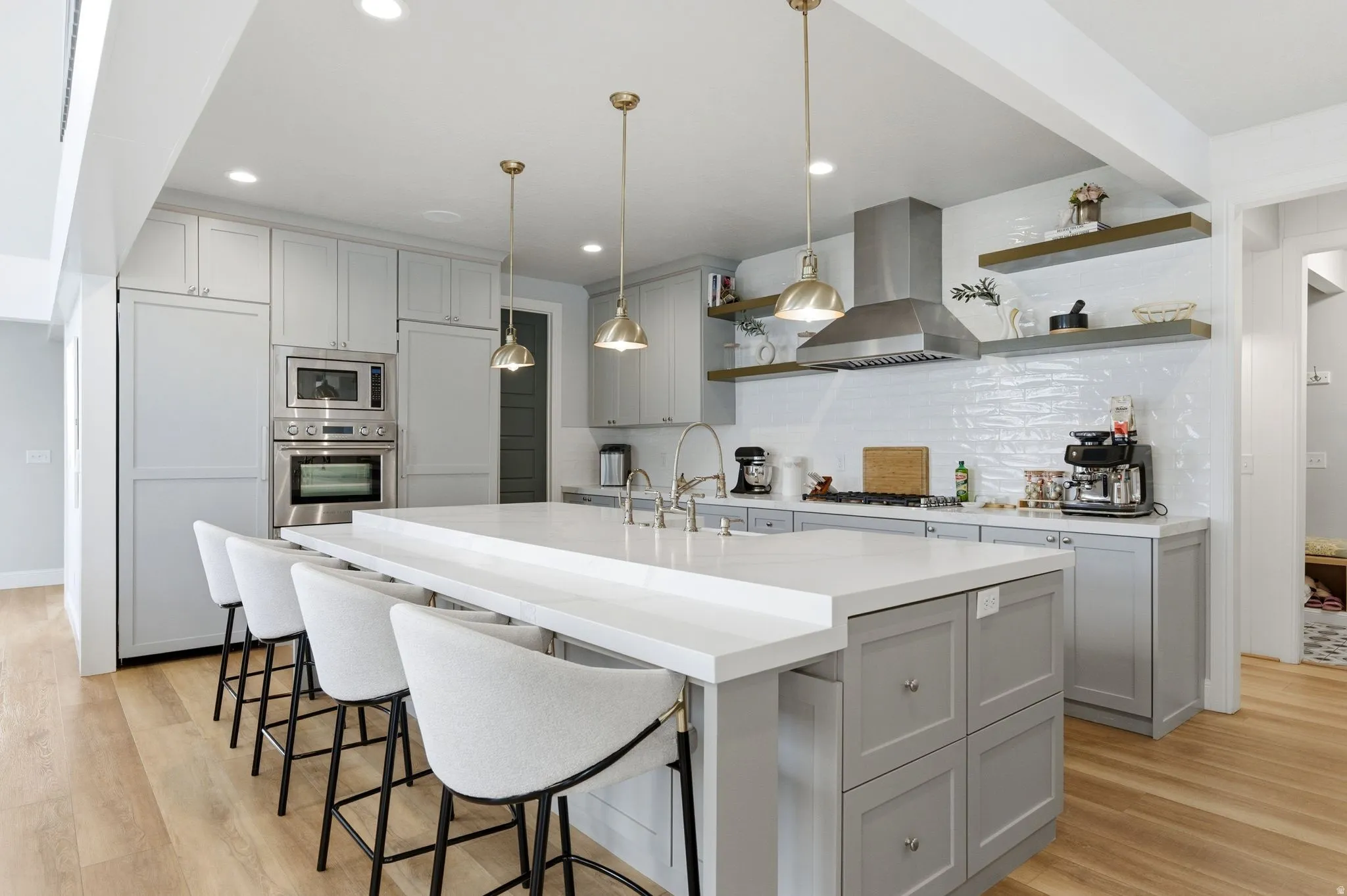 Kitchen featuring a breakfast bar area, pendant lighting, open shelves, gray cabinetry, and a kitchen island with sink