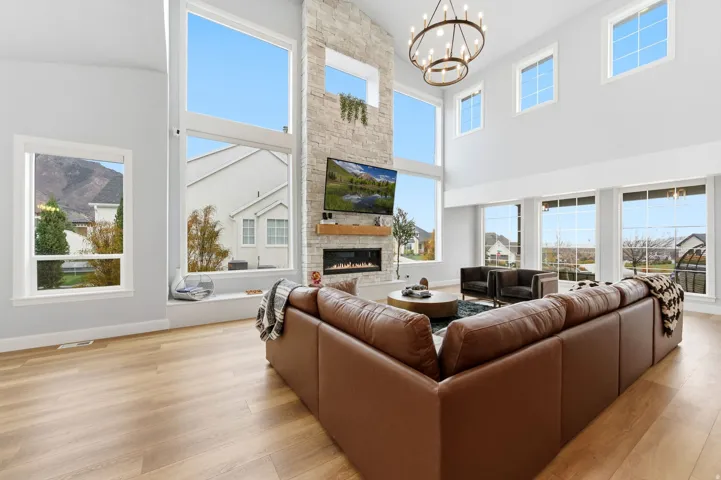 Living room with a stone fireplace, light wood finished floors, a chandelier, and a towering ceiling