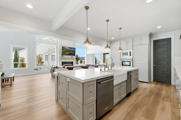 Kitchen with pendant lighting, light wood-style flooring, a fireplace, appliances with stainless steel finishes, and a kitchen island with sink