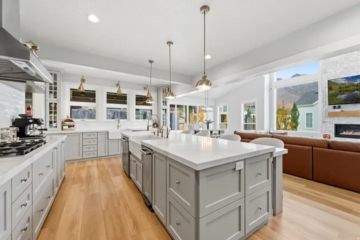Kitchen featuring glass insert cabinets, decorative light fixtures, gray cabinetry, wall chimney range hood, and open floor plan