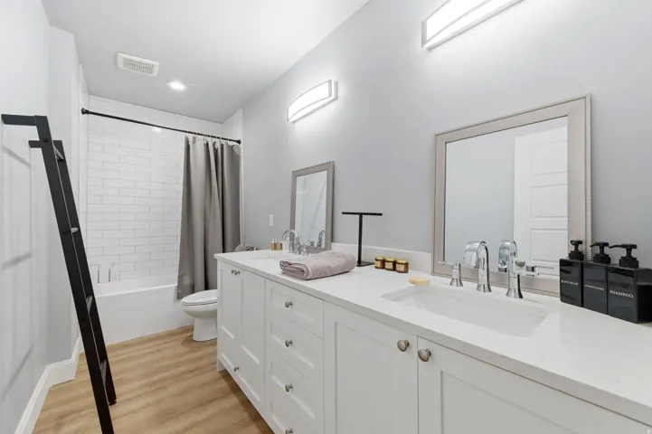 Full bathroom with shower / bath combination with curtain, double vanity, and light wood-style flooring
