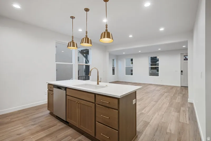 Kitchen featuring light wood-type flooring, hanging light fixtures, recessed lighting, stainless steel dishwasher, and open floor plan