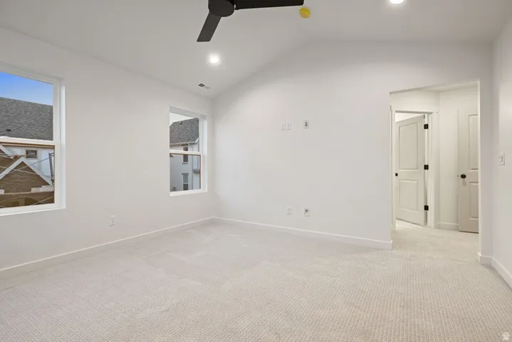 Carpeted empty room featuring lofted ceiling, recessed lighting, a ceiling fan, and plenty of natural light