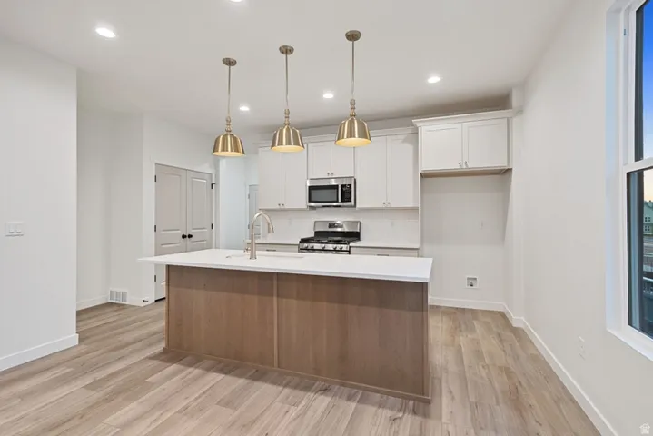 Kitchen featuring white cabinets, a kitchen island with sink, stainless steel appliances, pendant lighting, and tasteful backsplash
