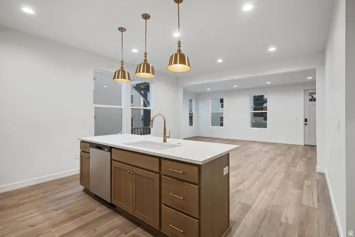 Kitchen featuring light wood-type flooring, hanging light fixtures, recessed lighting, stainless steel dishwasher, and open floor plan