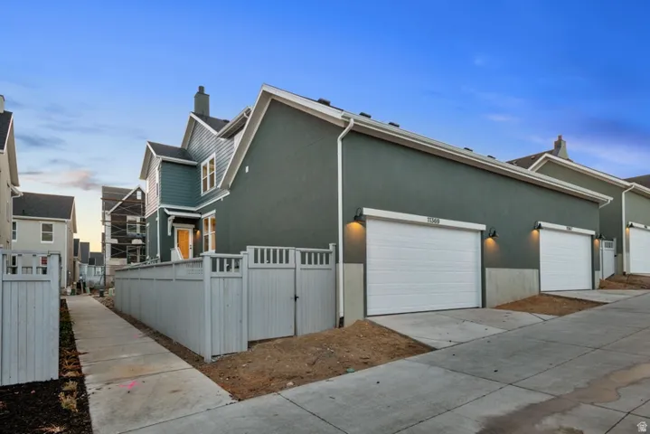 Property exterior at dusk with concrete driveway, stucco siding, a chimney, a gate, and a garage
