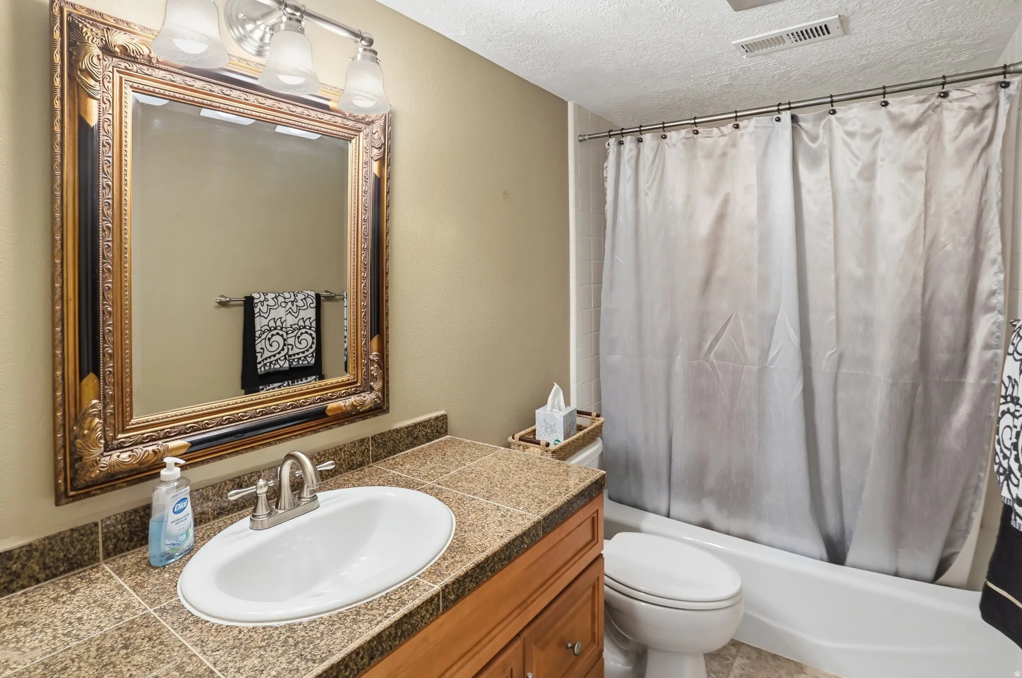 Bathroom with shower / tub combo with curtain, a textured ceiling, and vanity