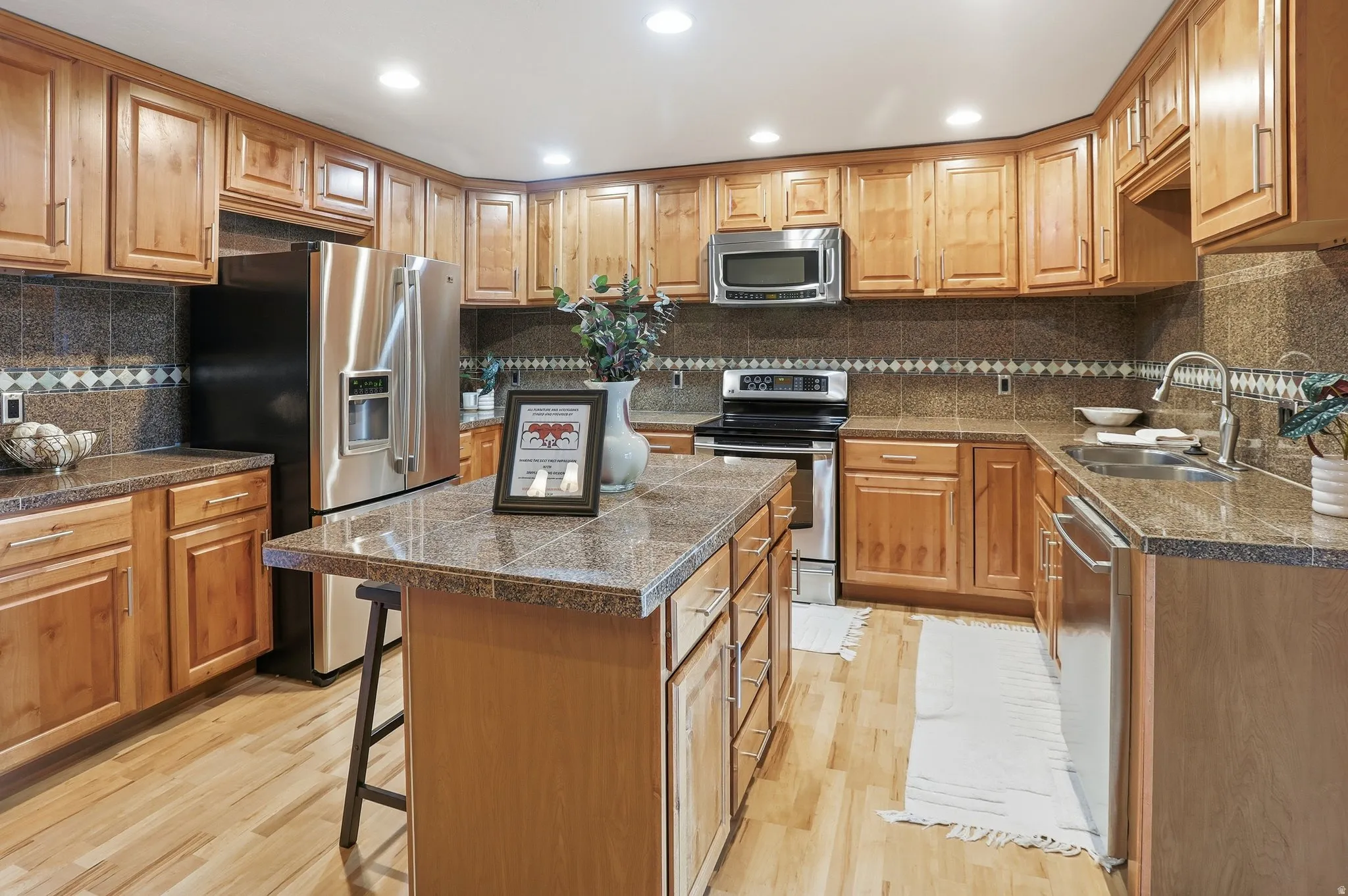 Kitchen with tile counters, a breakfast bar, stainless steel appliances, a kitchen island, and recessed lighting
