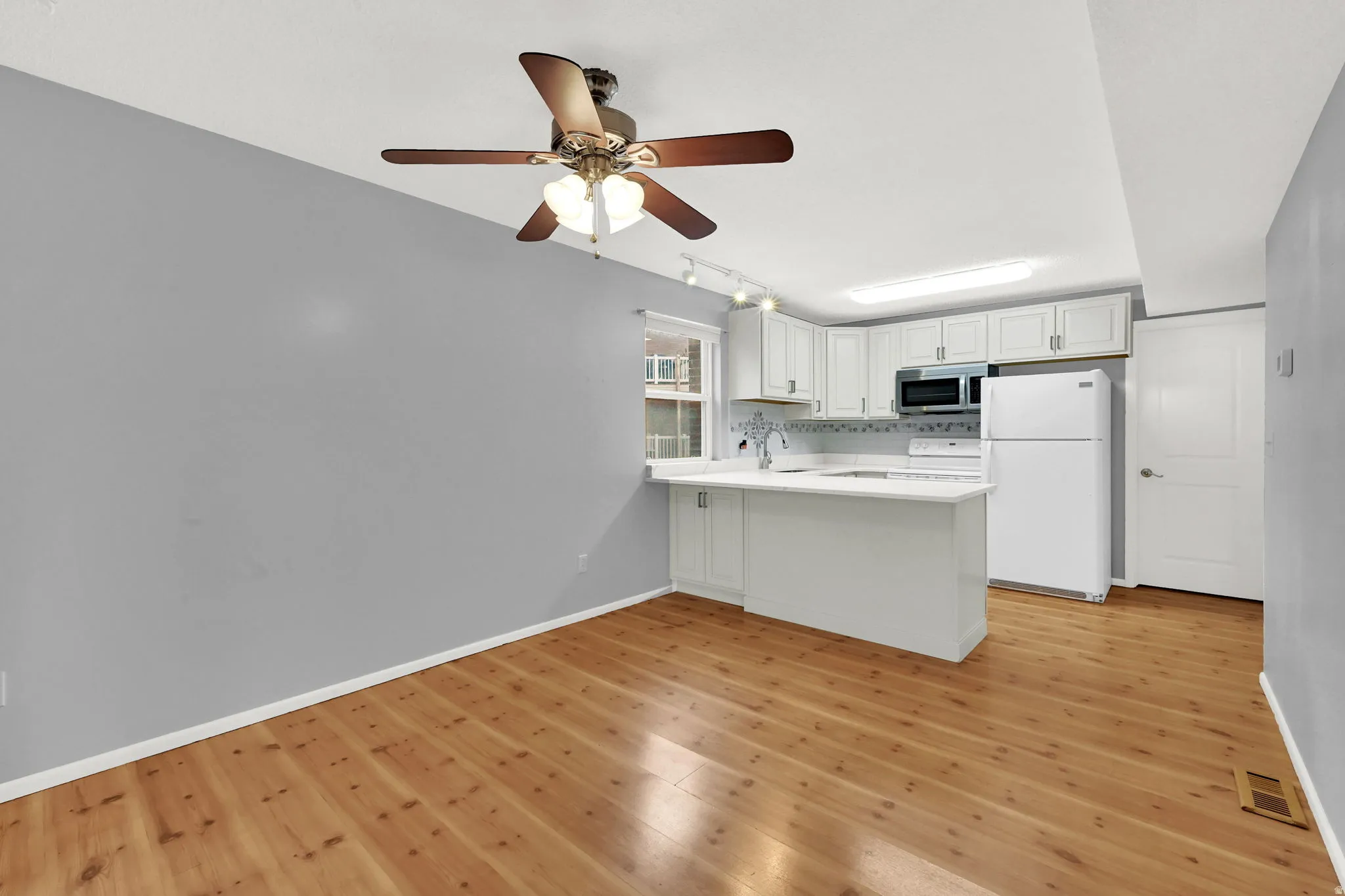Kitchen featuring light countertops, white appliances, white cabinetry, track lighting, and light wood-style flooring