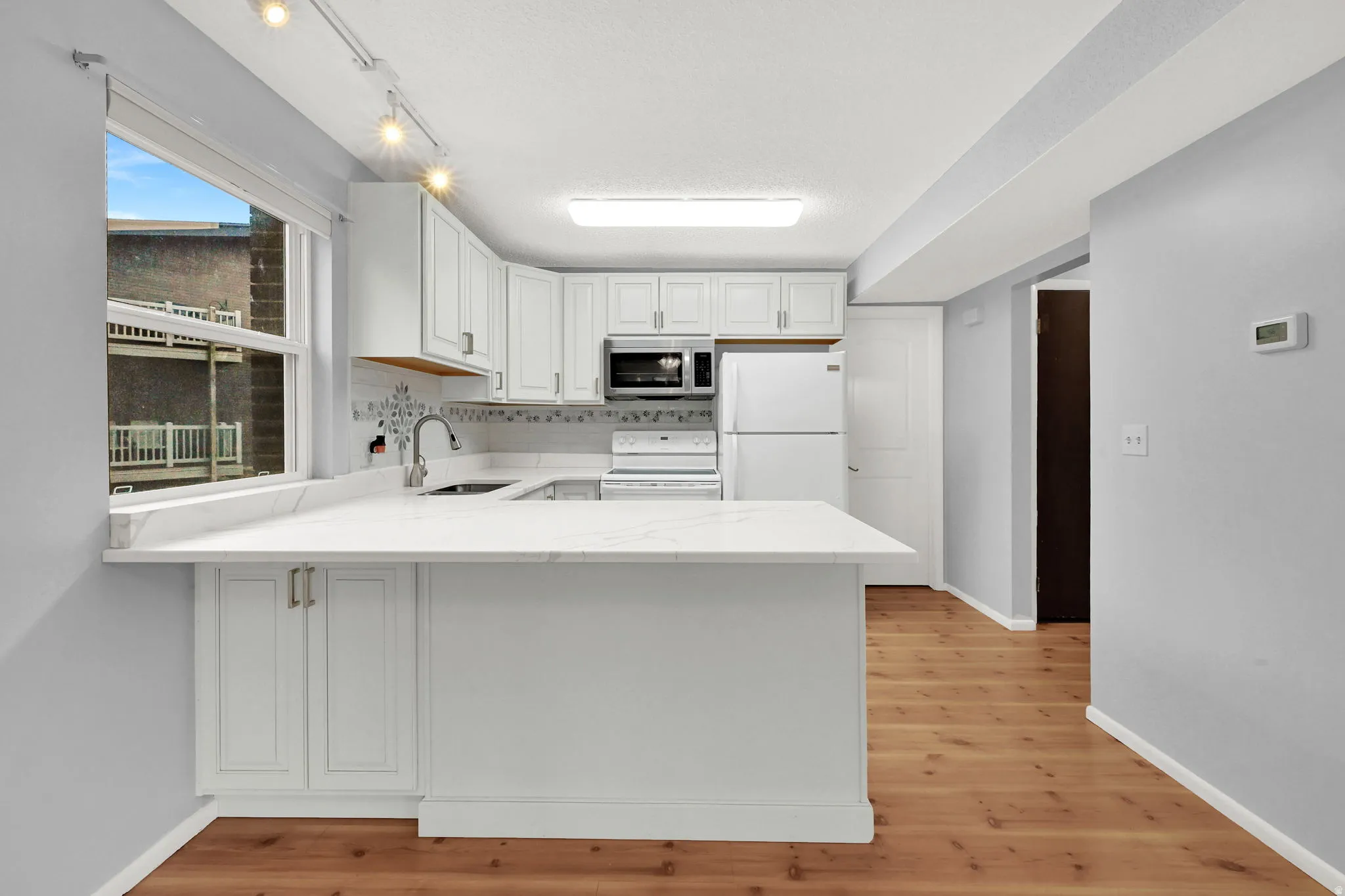 Kitchen featuring white cabinetry, white appliances, light wood-type flooring, and light stone countertops