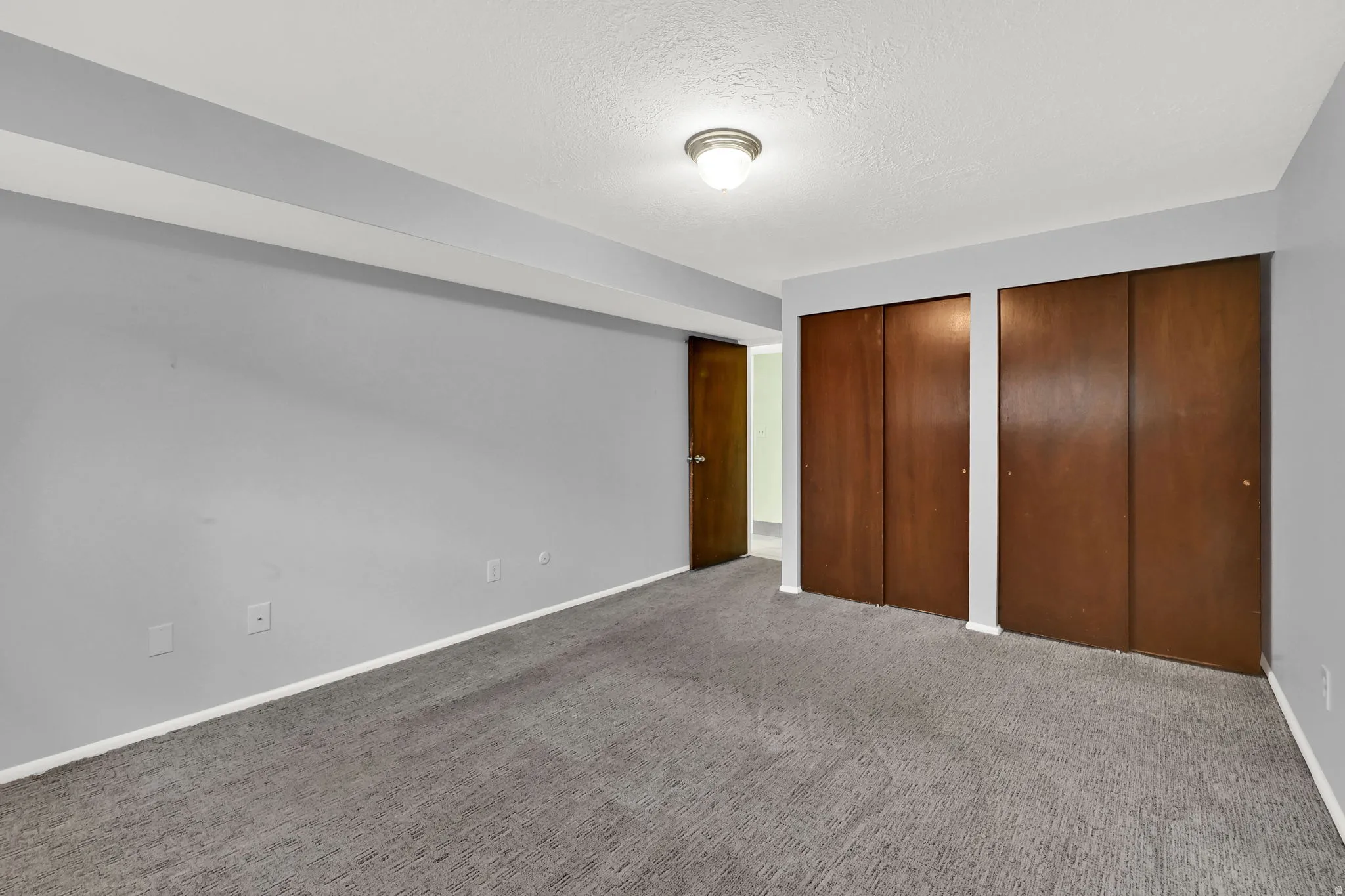 Unfurnished bedroom featuring a textured ceiling, multiple closets, and carpet