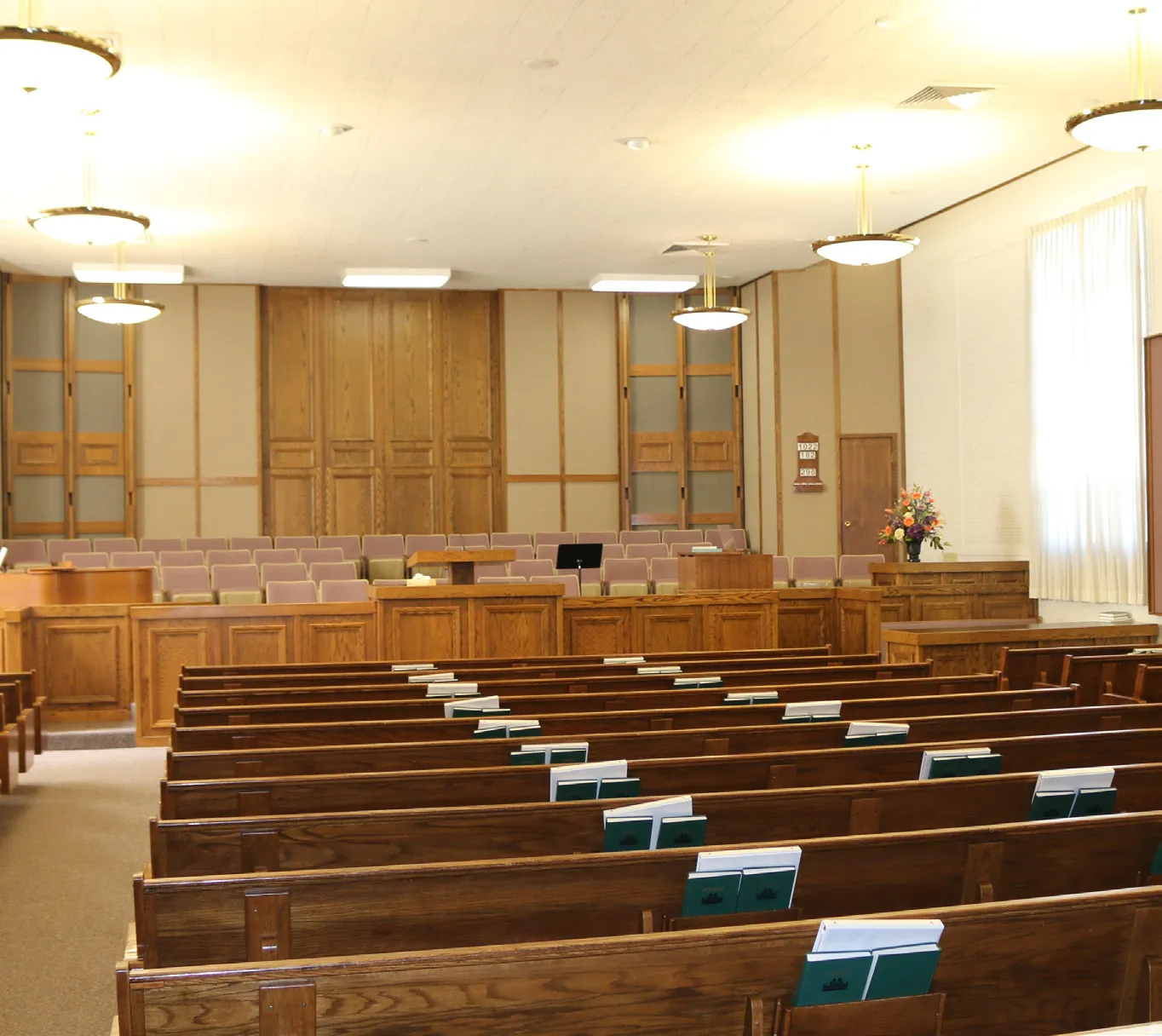 Chapel with upholstered wooden benches, pendant lighting, and a raised dais
