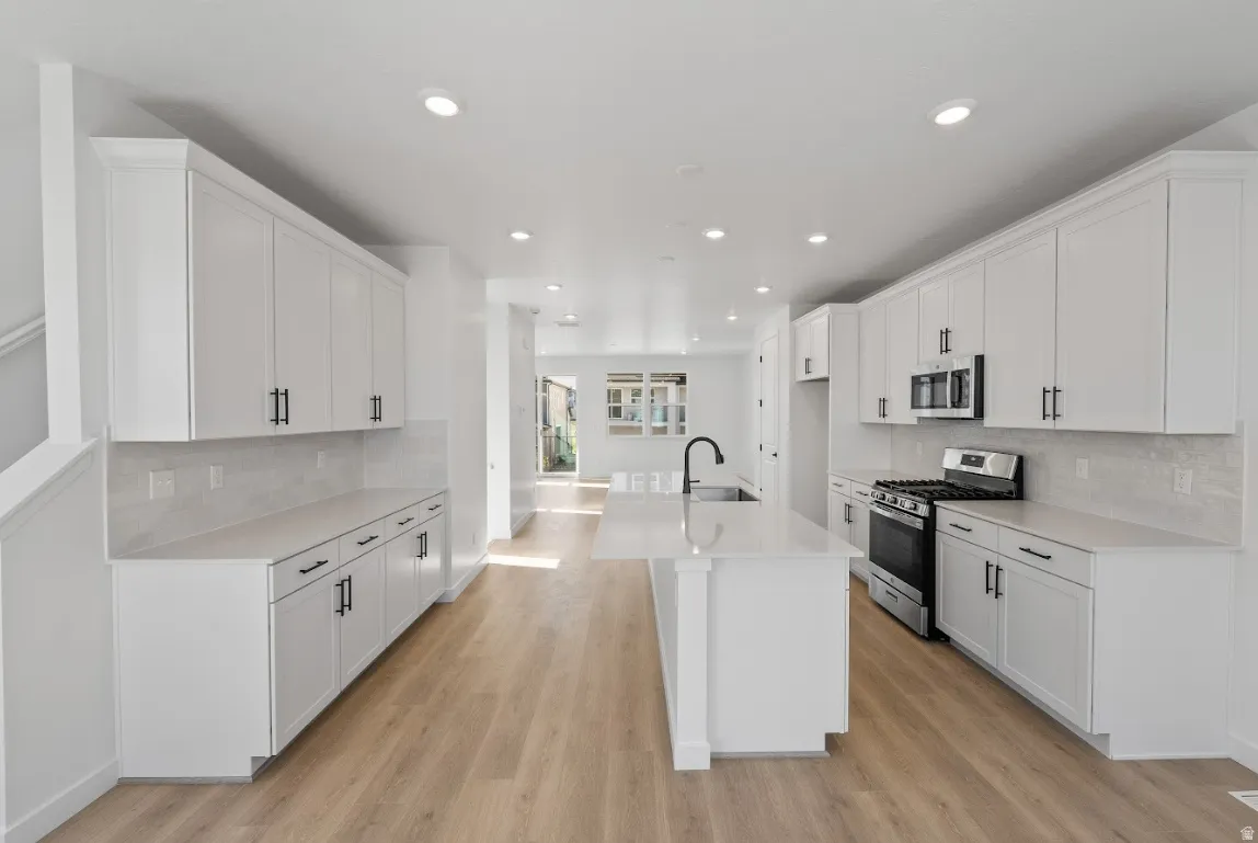 Kitchen featuring backsplash, appliances with stainless steel finishes, white cabinets, a center island with sink, and recessed lighting
