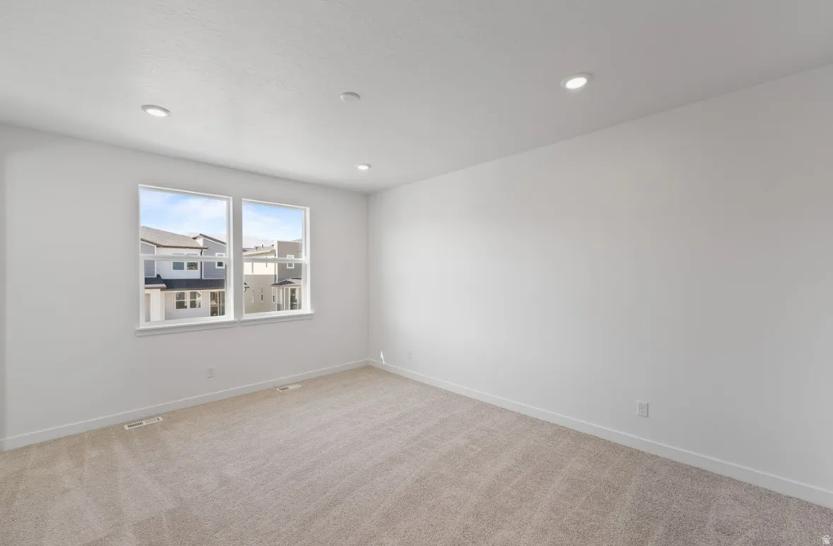 Empty room with light colored carpet and recessed lighting