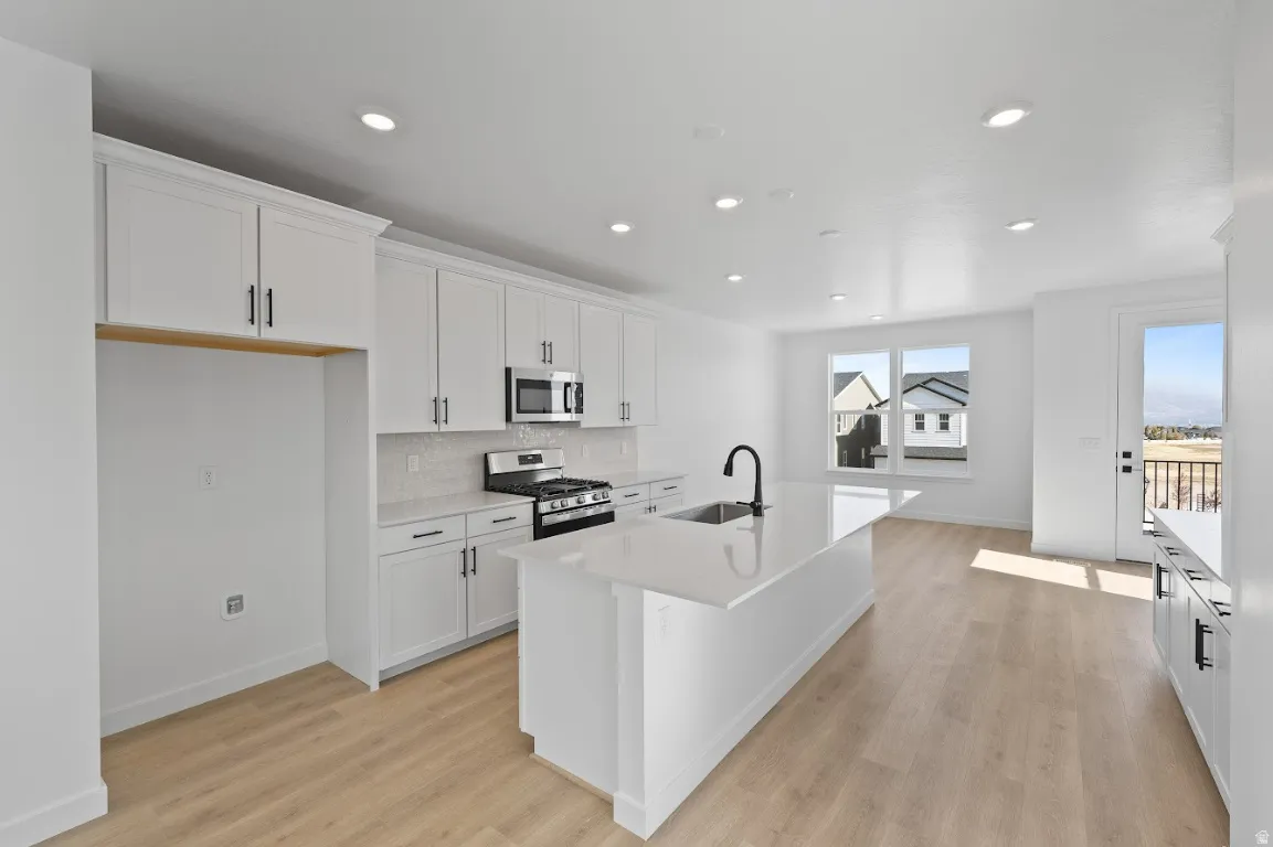 Kitchen with white cabinetry, appliances with stainless steel finishes, a kitchen island with sink, light wood finished floors, and recessed lighting