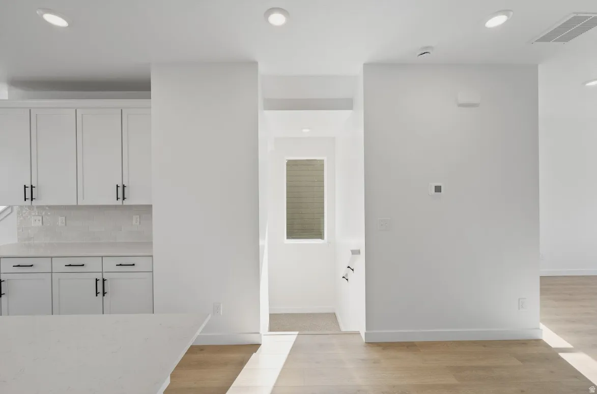 Kitchen featuring white cabinets, light wood-style floors, light stone countertops, decorative backsplash, and recessed lighting