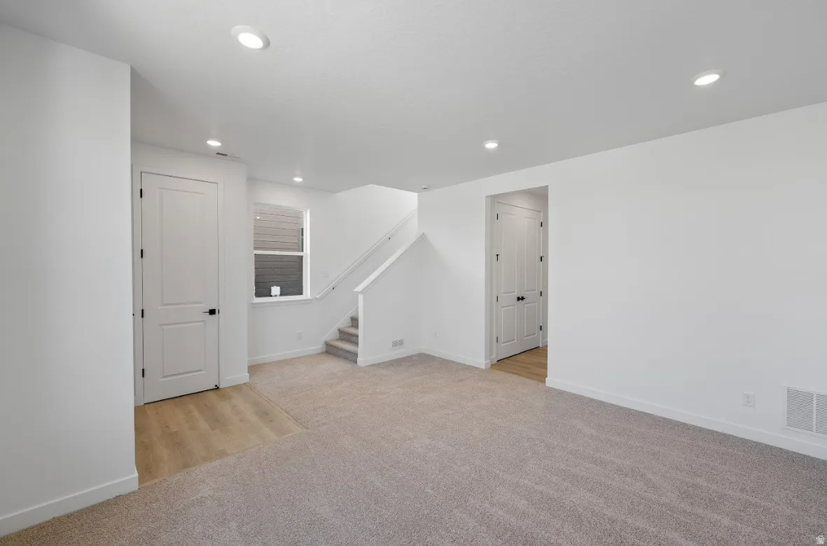 Below grade area with stairway, light colored carpet, recessed lighting, and light wood-style flooring