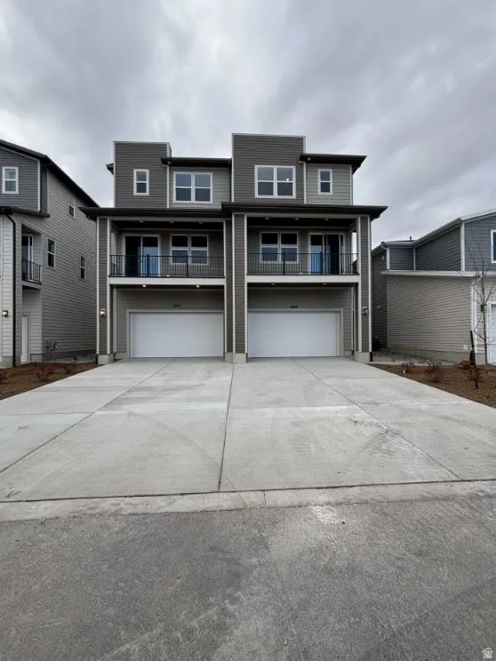 View of front facade featuring a balcony, driveway, and a garage
